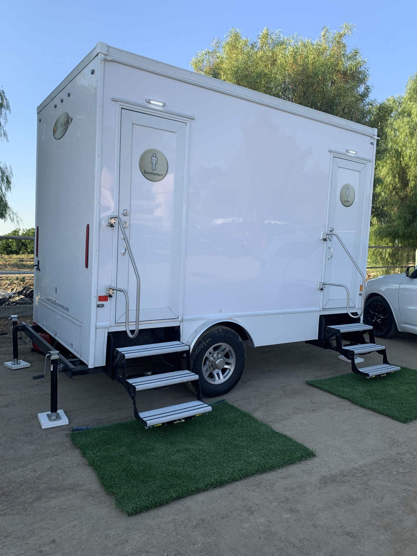 Premium restroom trailer set up at an outdoor event with grass mats at entrances
